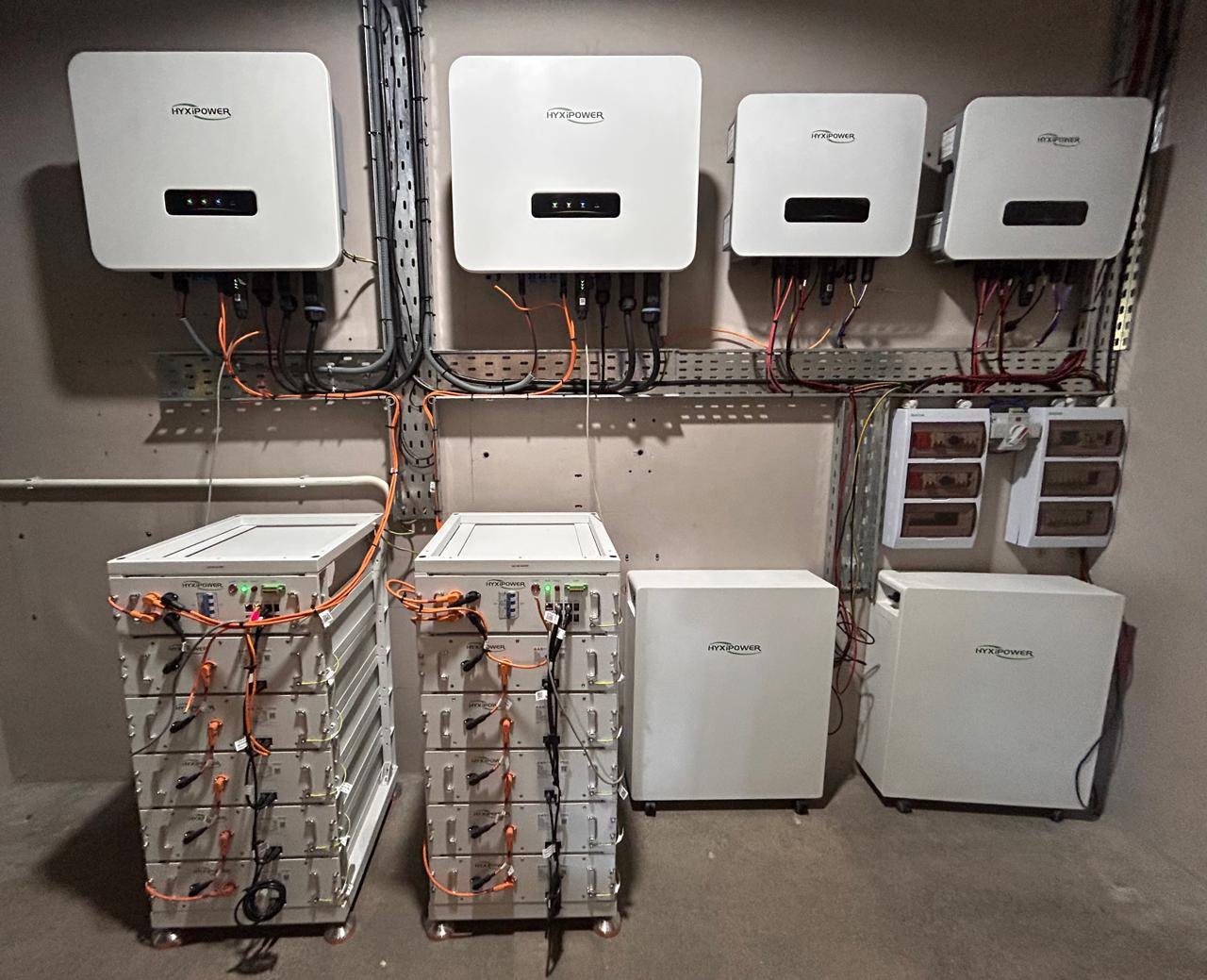Four Hyxipower solar inverters above two high-voltage battery racks with orange DC cabling at the Solarex Experience Center