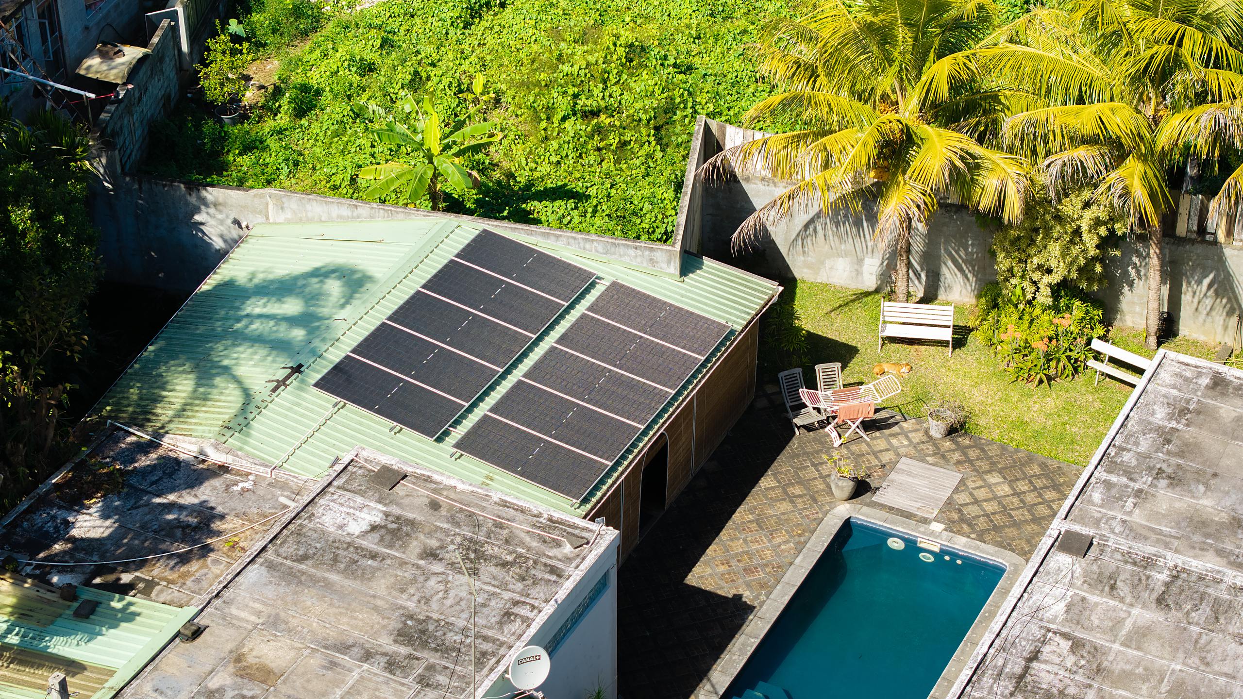 Aerial view of ten bifacial solar panels mounted parallel to the inclined tin roof of a Mauritian family home